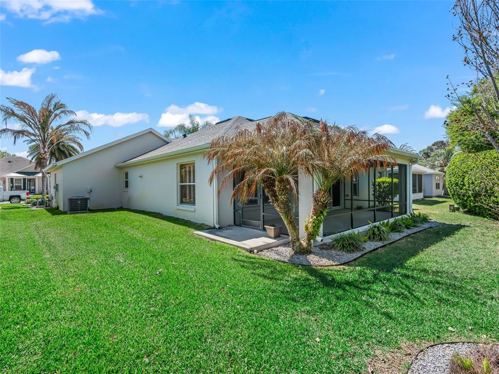 The exterior of a house features a screened-in patio, a palm tree, and a lawn — 1569 OLAR COURT, THE VILLAGES, FL