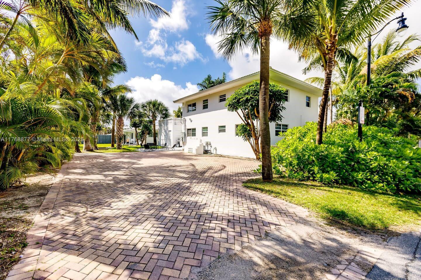 A white two-story house stands behind a large brick-paved driveway surrounded by palm trees — 18825 Atlantic Blvd, Sunny Isles Beach FL 33160, SUNNY ISLES BEACH, FL