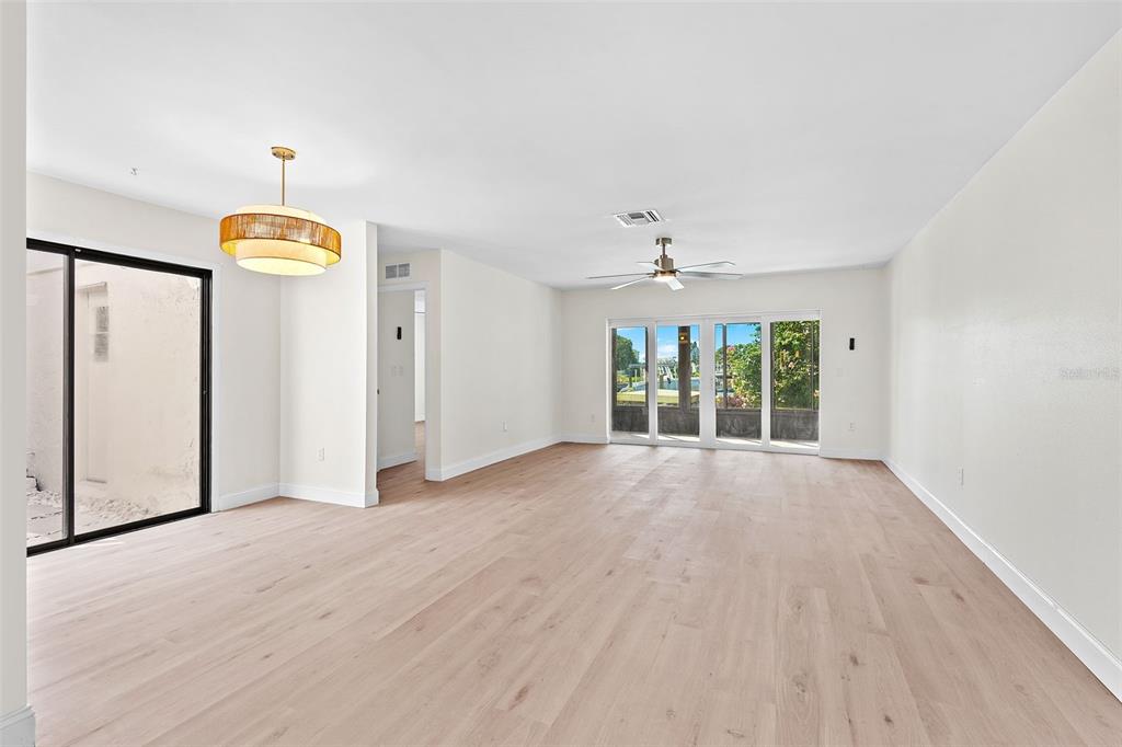 A spacious, minimalist living area with light wood floors, a modern chandelier, and sliding glass doors — 4448 MARINE PARKWAY, NEW PORT RICHEY, FL