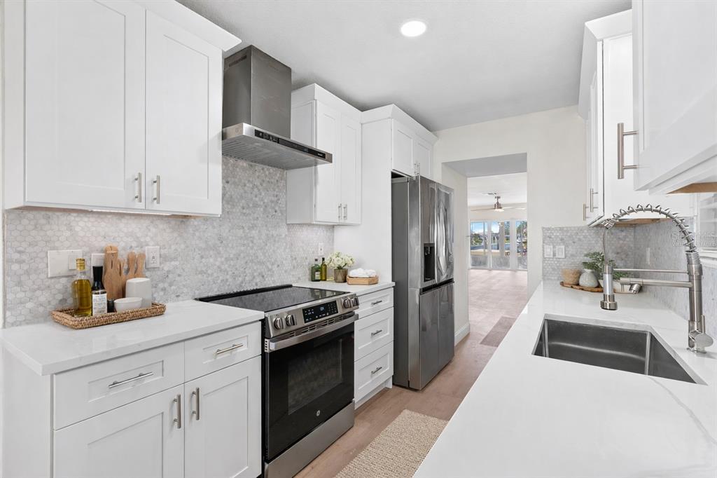 A modern kitchen features white cabinets, stainless steel appliances, and a light-colored hexagon tile backsplash — 4448 MARINE PARKWAY, NEW PORT RICHEY, FL