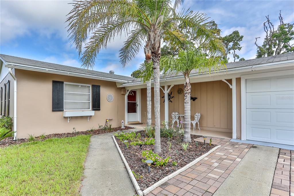 A single-story house exterior features a tan facade, a covered porch, and two palm trees — 7163 FIRESIDE STREET, SPRING HILL, FL