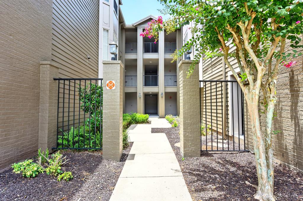 A concrete walkway leads through a gated entrance toward a three-story apartment building exterior — 420 SUMMIT RIDGE PLACE UNIT 316, LONGWOOD, FL