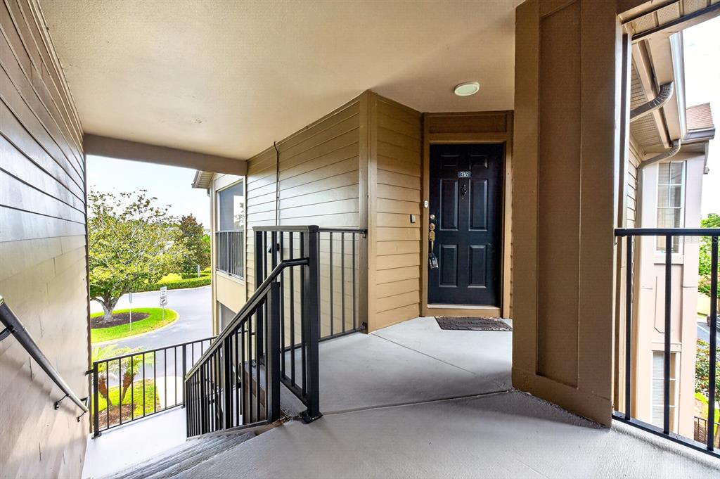 An exterior view of a second-story apartment landing with stairs, a black door, and railings — 420 SUMMIT RIDGE PLACE UNIT 316, LONGWOOD, FL