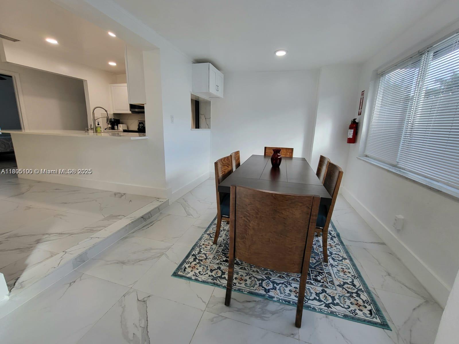 A dining area features a dark wood table, chairs, and a patterned rug on marble flooring — FORT LAUDERDALE, FL