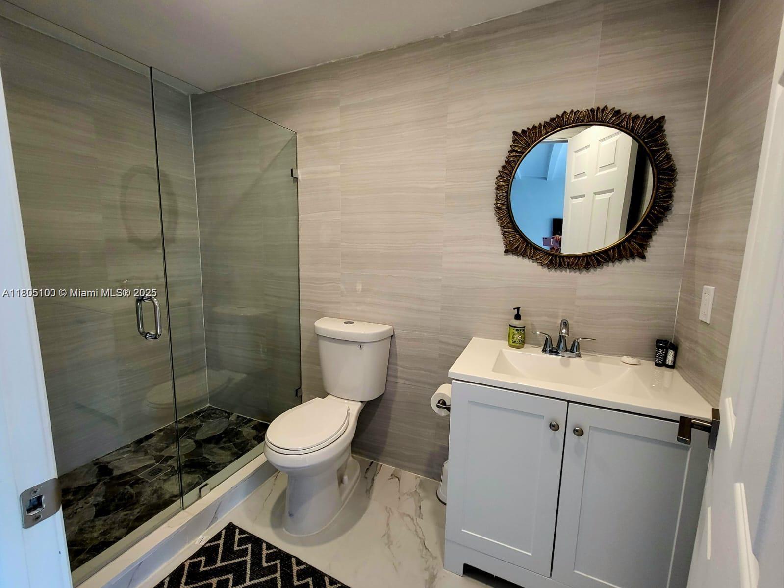 A bathroom features a glass-enclosed shower, a white vanity, and a decorative round mirror — FORT LAUDERDALE, FL