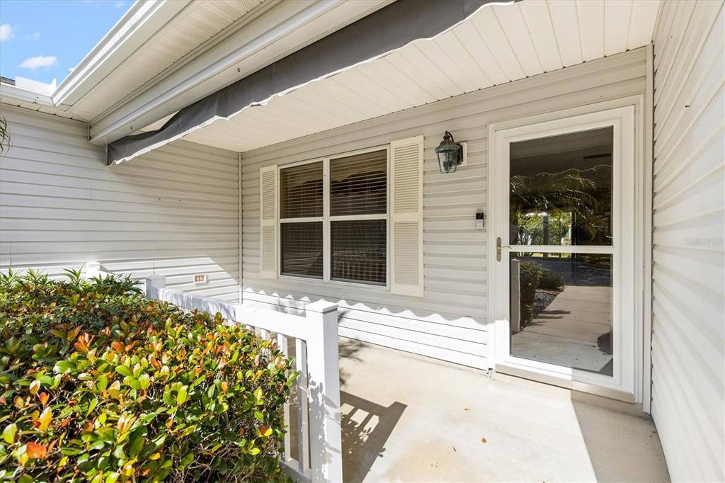 A covered front porch features light-colored siding, a glass storm door, and a white railing — 9711 SE 171ST ARGYLL STREET, THE VILLAGES, FL