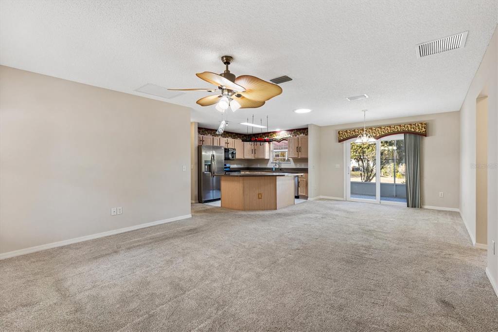 A spacious living room with beige carpet opens to a kitchen with wood cabinets — 9711 SE 171ST ARGYLL STREET, THE VILLAGES, FL