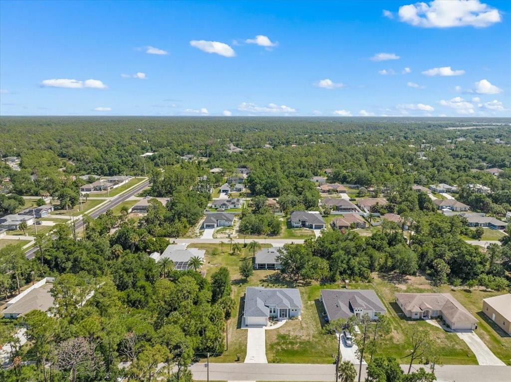 An aerial view shows several suburban houses surrounded by dense trees under a blue sky — WOODWARD AVENUE, NORTH PORT, FL