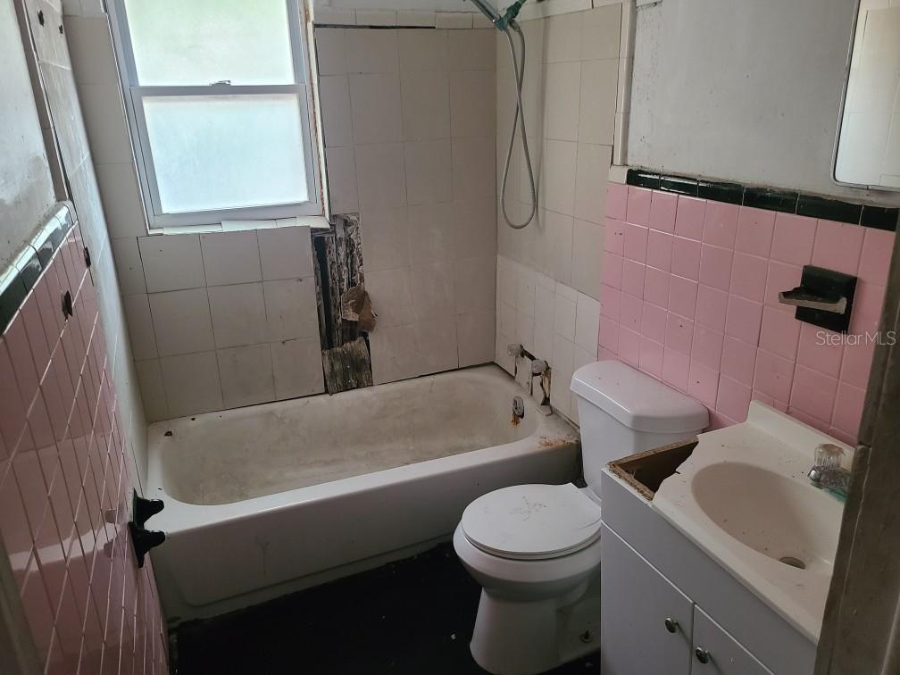 A bathroom features a bathtub with missing wall tiles, a toilet, and a vanity sink — 1127 ROBINSON AVENUE, APOPKA, FL