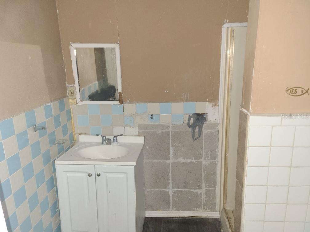 A bathroom features a white vanity, a small mirror, and walls with partial tile work — 1127 ROBINSON AVENUE, APOPKA, FL