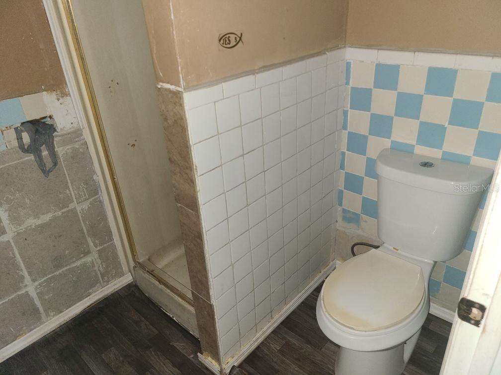 A bathroom features a shower stall, a toilet, and walls with blue and white tiles — 1127 ROBINSON AVENUE, APOPKA, FL