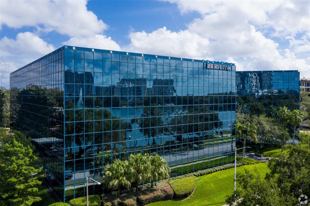 A multi-story office building with a glass facade reflects the surrounding trees and lake — 225 E ROBINSON STREET, ORLANDO, FL