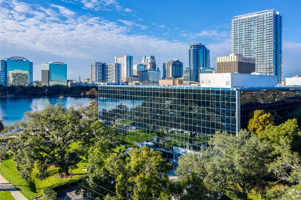 An exterior view of a glass-walled office building overlooking a lake and city skyline — 225 E ROBINSON STREET, ORLANDO, FL