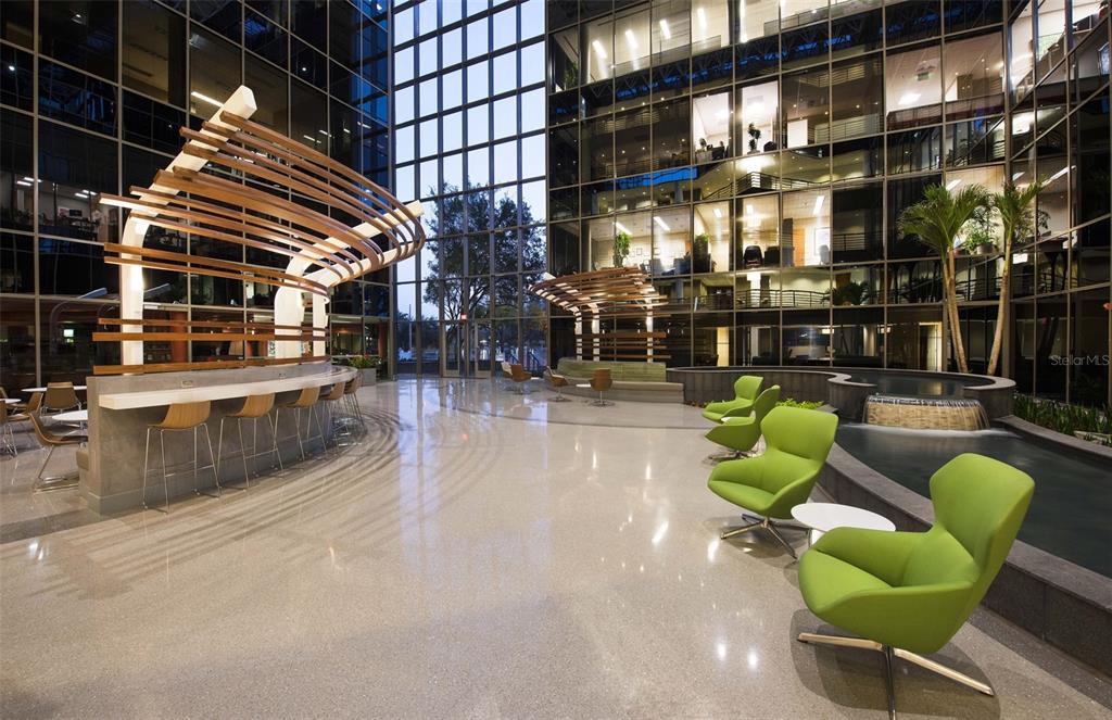 A modern office building atrium features a curved wooden canopy, bar seating, and green chairs — 225 E ROBINSON STREET, ORLANDO, FL