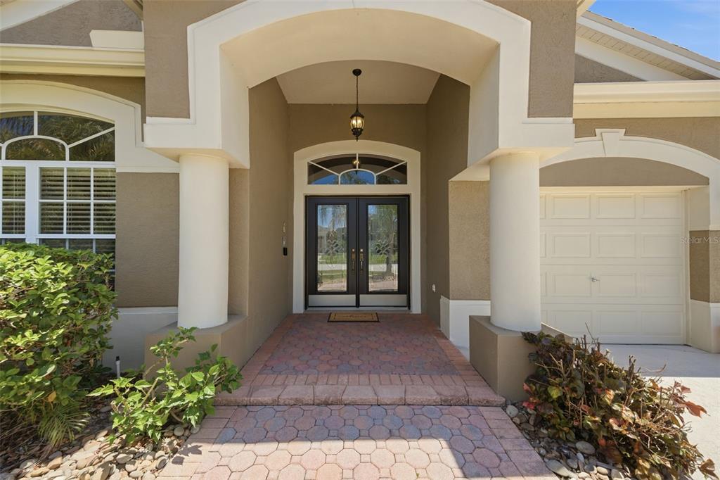 A covered entryway features a brick paver walkway, double front doors, and two white columns — 25946 RISEN STAR DRIVE, WESLEY CHAPEL, FL