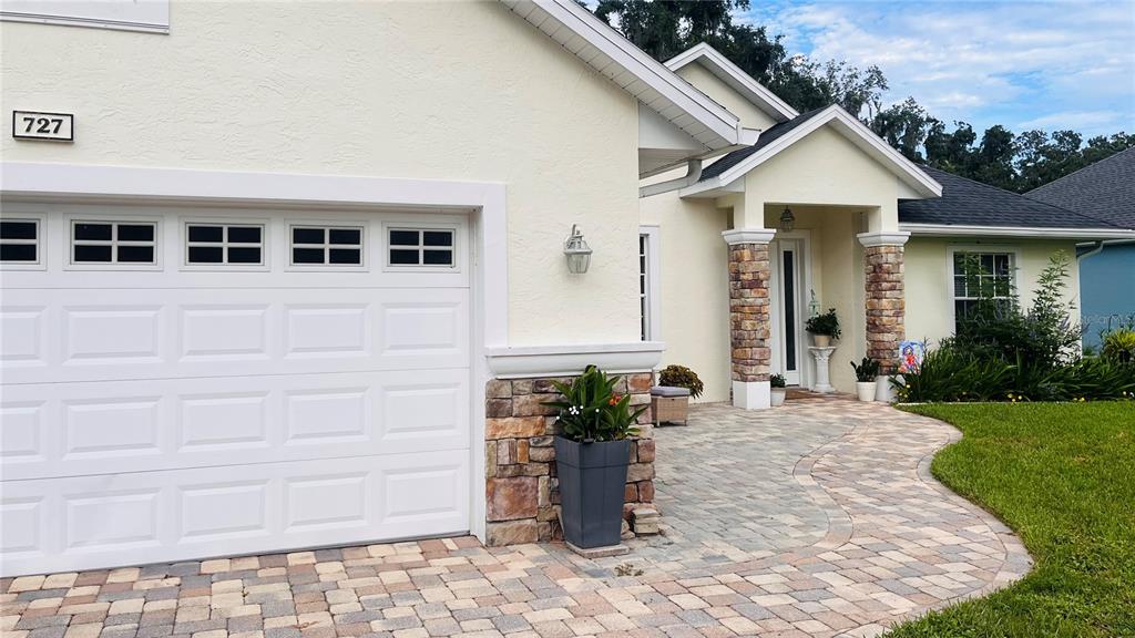 A beige house exterior features a white garage door, stone accents, and a paved walkway — 727 ALDENWOOD TRAIL, NEW SMYRNA BEACH, FL