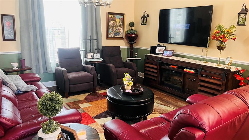 A living room features red leather sofas, two armchairs, a round ottoman, and a television — 727 ALDENWOOD TRAIL, NEW SMYRNA BEACH, FL