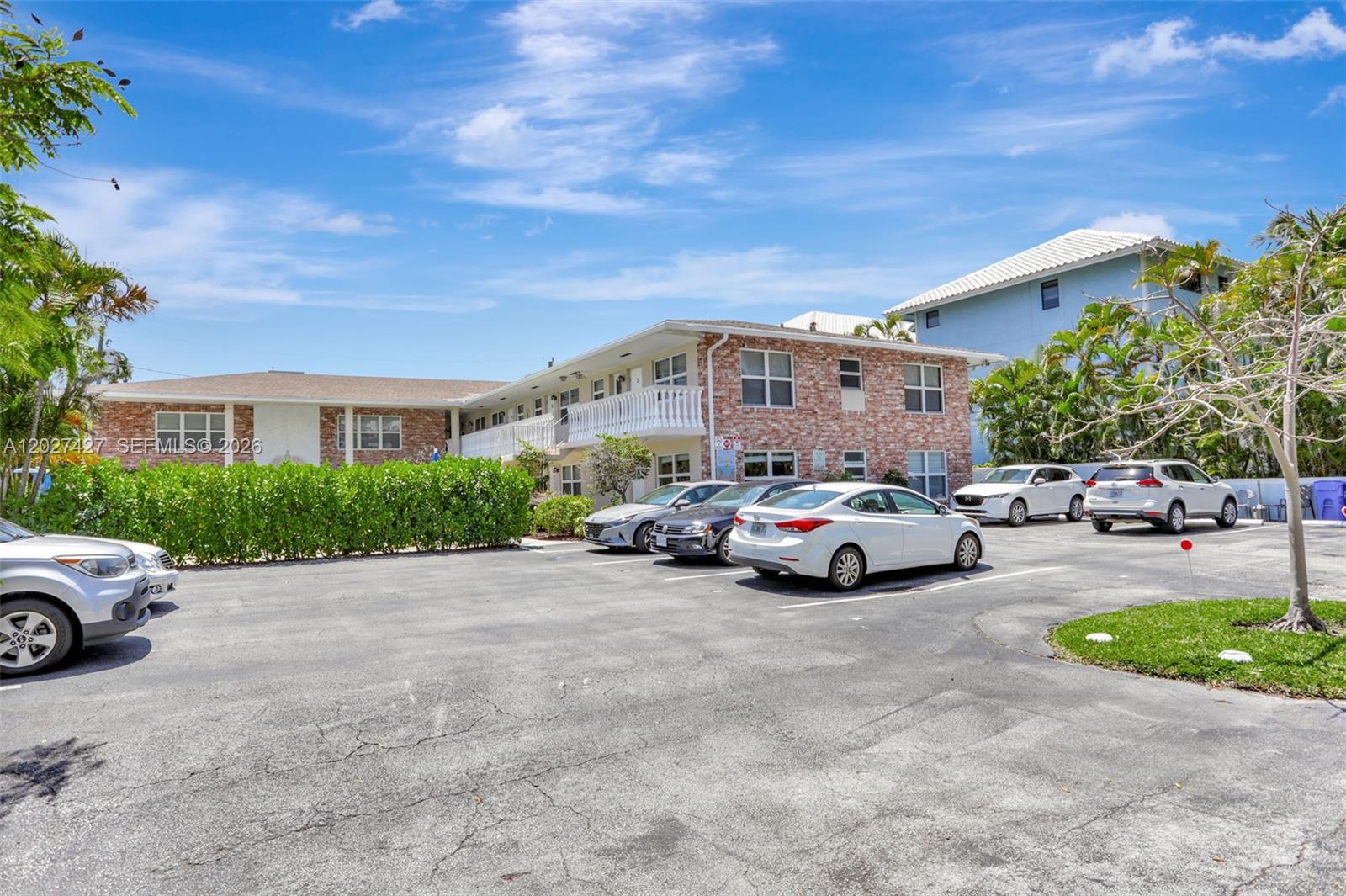 A two-story brick apartment building features a parking lot with several cars in front — POMPANO BEACH, FL
