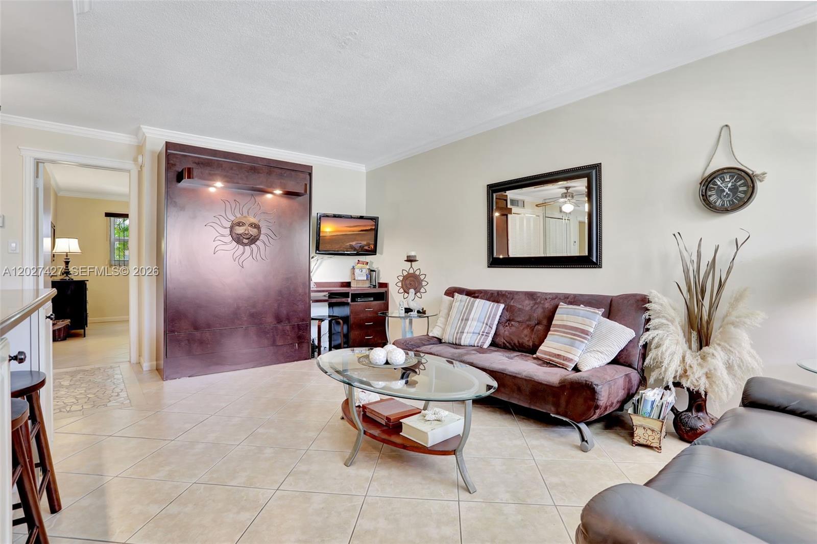 A living room features a brown sofa, a glass coffee table, and a wall-mounted Murphy bed — POMPANO BEACH, FL