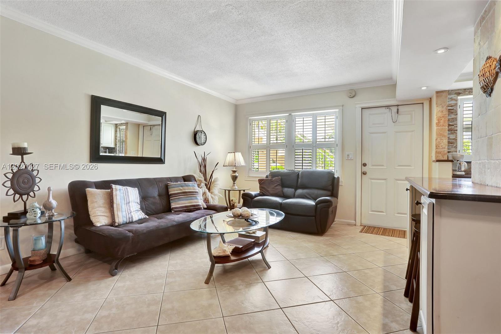 A living room features a dark sofa, a glass coffee table, and tile flooring — POMPANO BEACH, FL