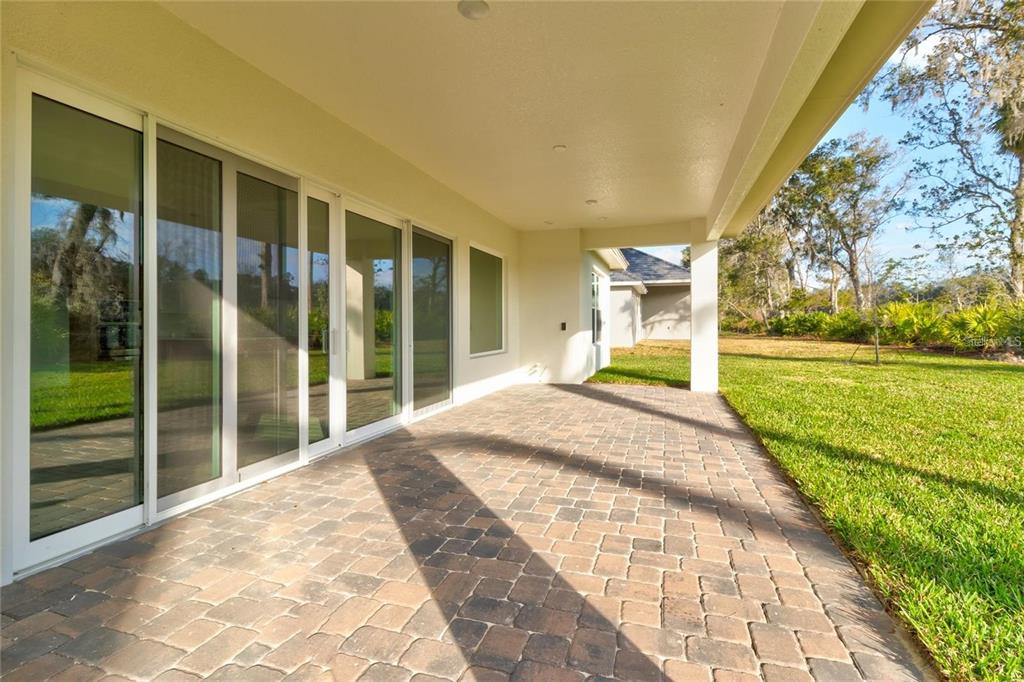 A covered patio features paver flooring and large sliding glass doors overlooking a grassy yard — 74 NEW LEATHERWOOD DRIVE, PALM COAST, FL