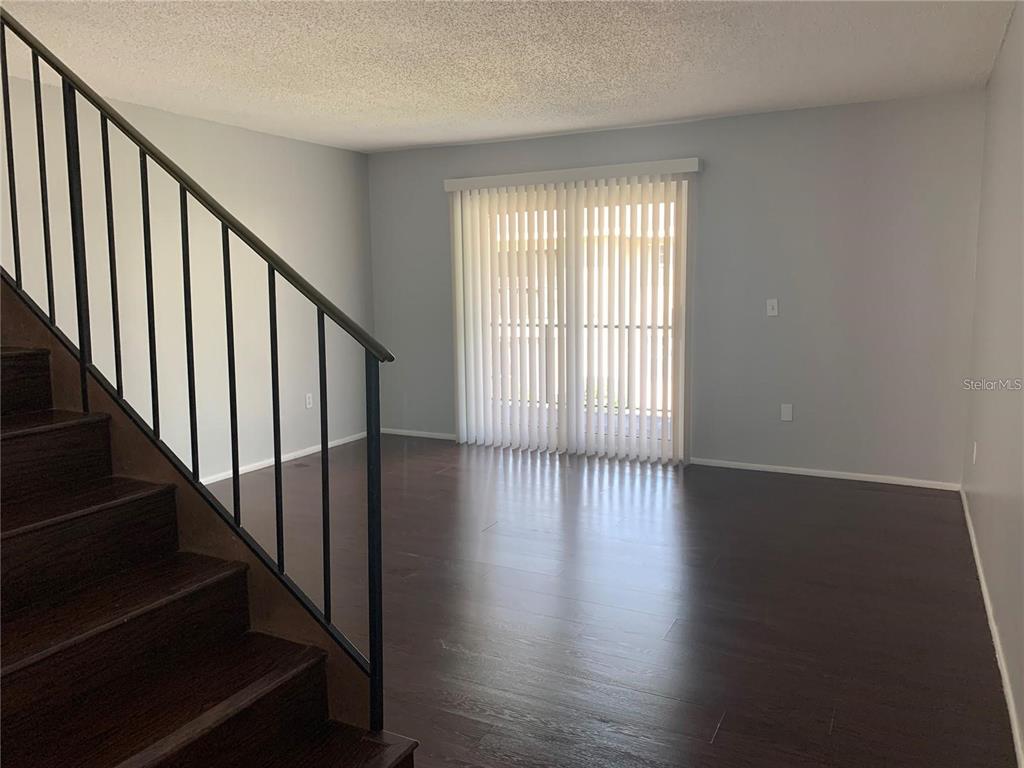 A living room features dark wood flooring, a staircase with a black railing, and vertical blinds — 14402 REUTER STRASSE CIRCLE UNIT #2, TAMPA, FL