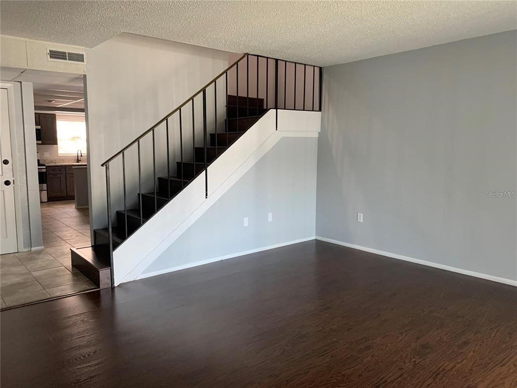 A living room features dark wood flooring, a staircase with metal railings, and grey walls — 14402 REUTER STRASSE CIRCLE UNIT #2, TAMPA, FL