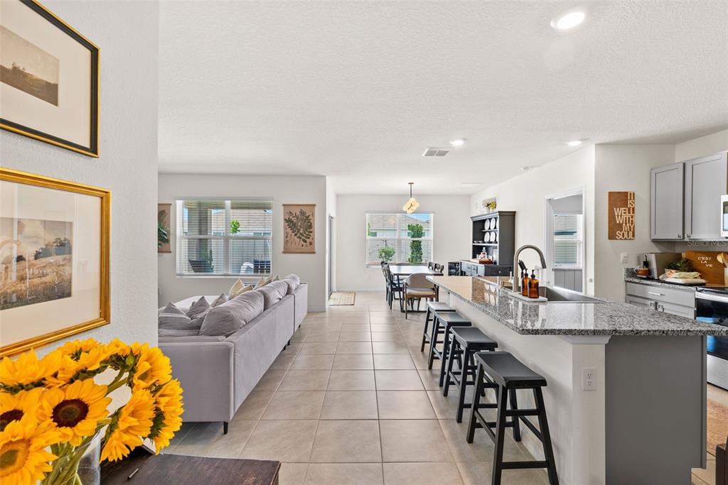 An open-concept kitchen with a granite island and bar stools overlooks a living and dining area — 33607 HAMILTON HILL LANE, WESLEY CHAPEL, FL