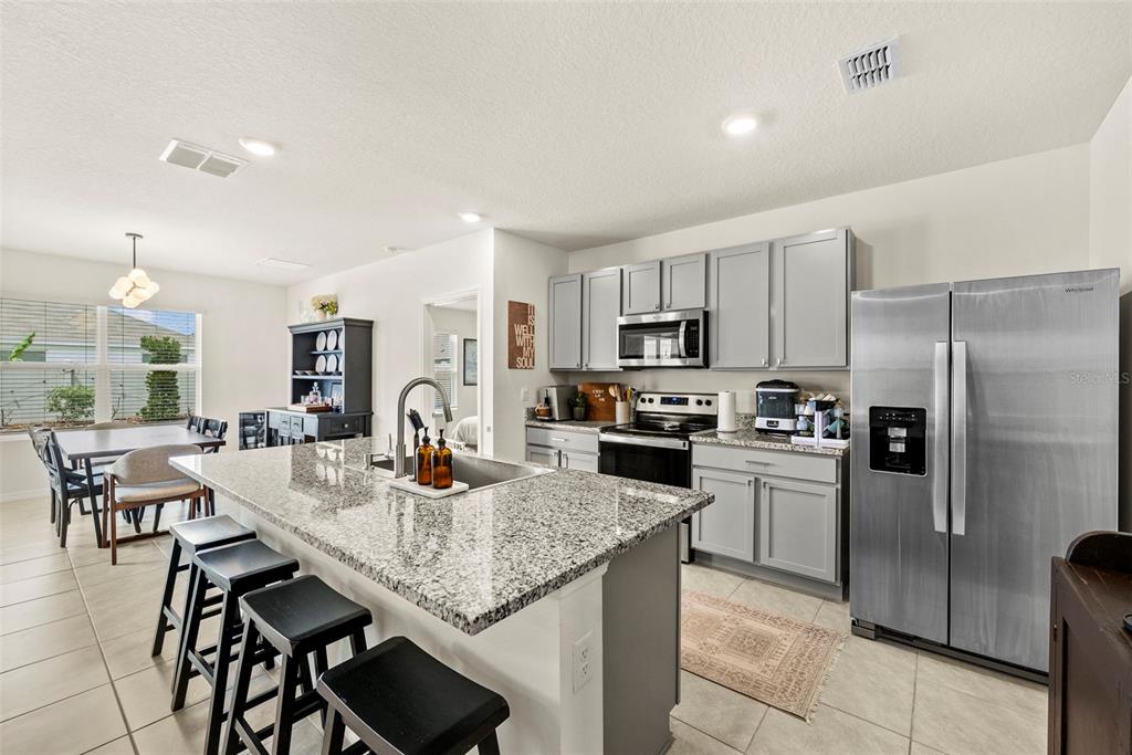 A kitchen features gray cabinets, granite countertops, a large island with bar seating, and stainless-steel appliances — 33607 HAMILTON HILL LANE, WESLEY CHAPEL, FL
