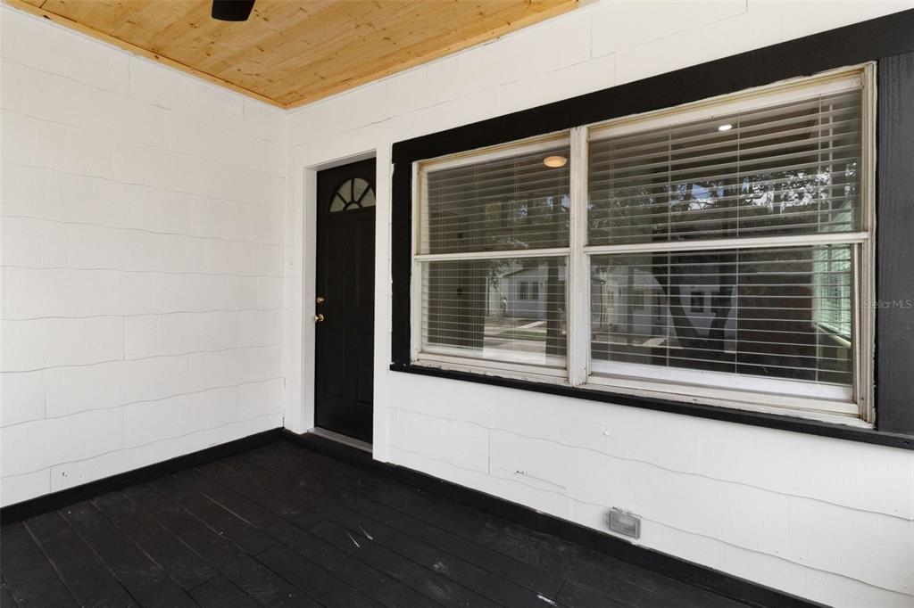 A covered porch features white paneled walls, a black door, and a dark wooden floor — 2329 W BEACH STREET, TAMPA, FL