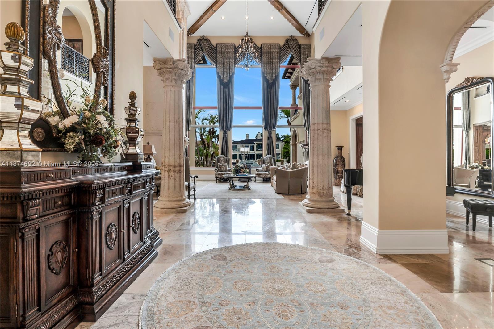 A grand foyer with marble floors, stone columns, and a large window overlooking a pool — 700 Osprey Point Cir, Boca Raton FL 33431, BOCA RATON, FL