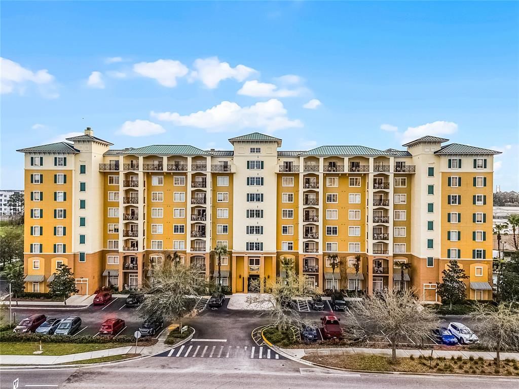 An exterior view of a multi-story yellow apartment building with balconies and a parking lot — 8100 POINCIANA BOULEVARD UNIT 2501, ORLANDO, FL