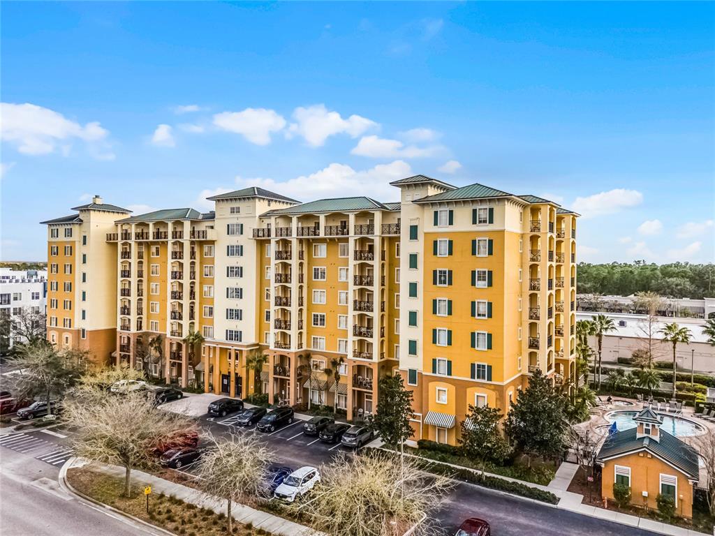 A multi-story yellow apartment building with a parking lot and a small pool area — 8100 POINCIANA BOULEVARD UNIT 2501, ORLANDO, FL