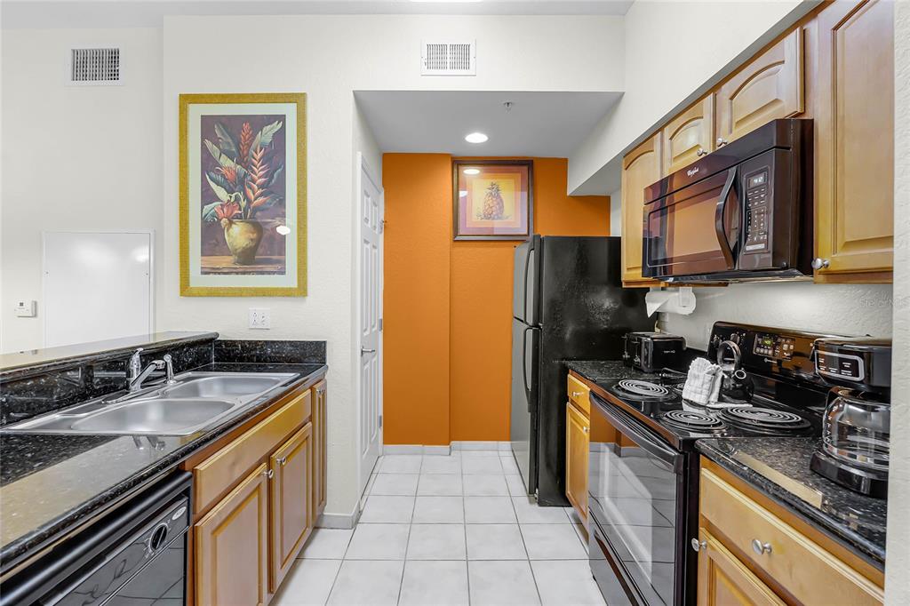 A kitchen features wood cabinets, black appliances, granite countertops, and a white tiled floor — 8100 POINCIANA BOULEVARD UNIT 2501, ORLANDO, FL