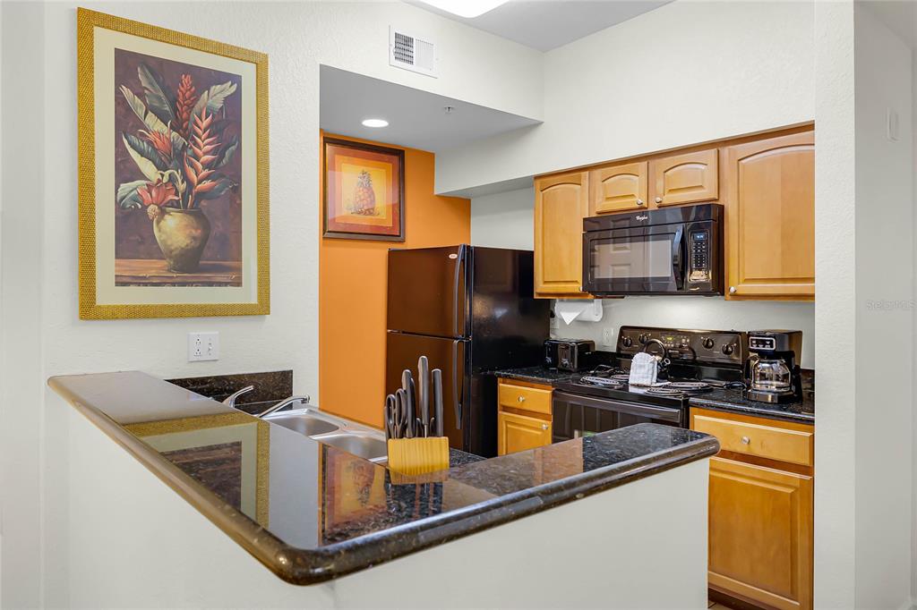 A kitchen features wood cabinets, black appliances, granite countertops, and a breakfast bar — 8100 POINCIANA BOULEVARD UNIT 2501, ORLANDO, FL