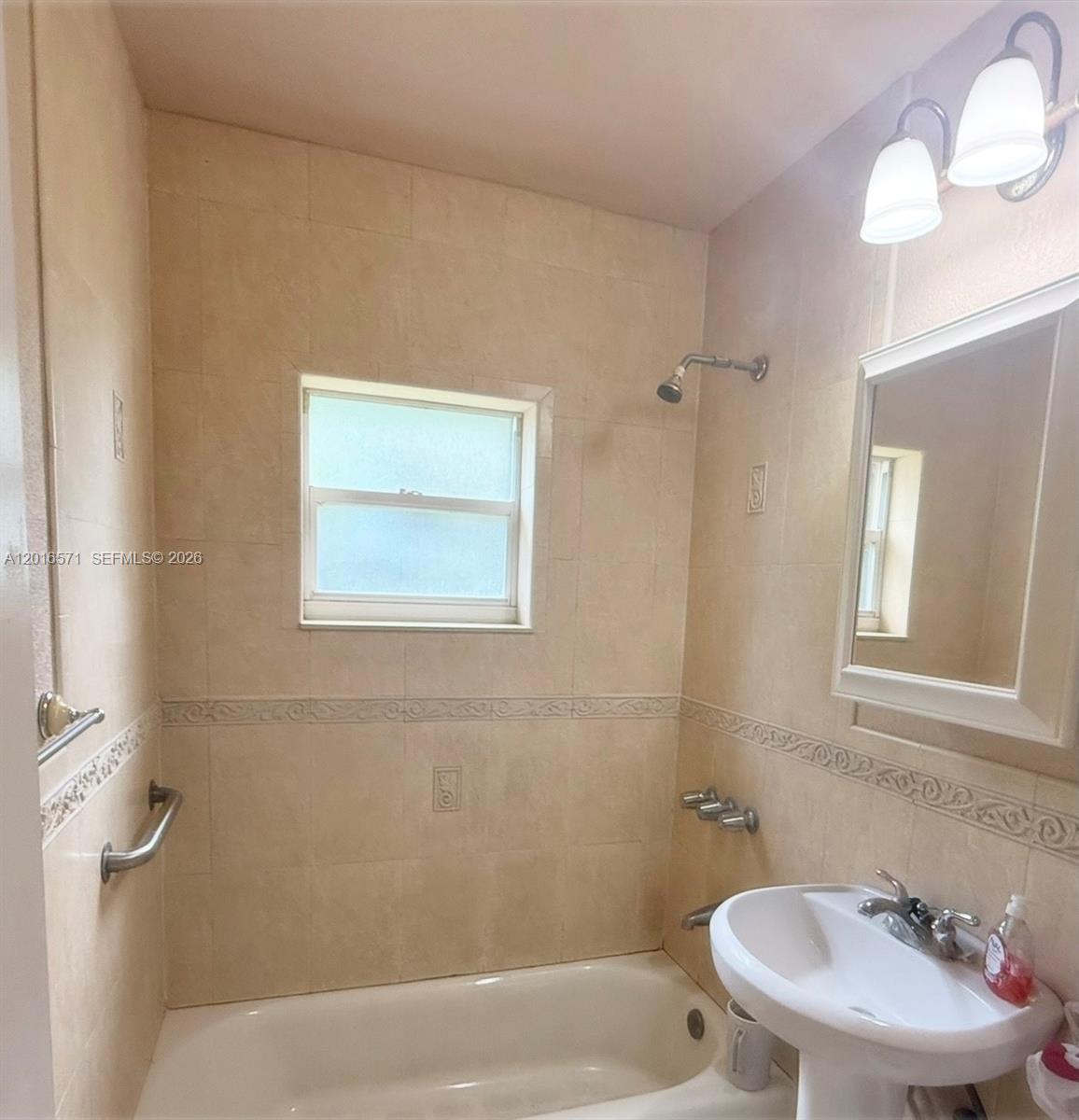 A bathroom features a pedestal sink, a bathtub with a showerhead, and beige tiled walls — 50 E 44th St, Hialeah FL 33013, HIALEAH, FL