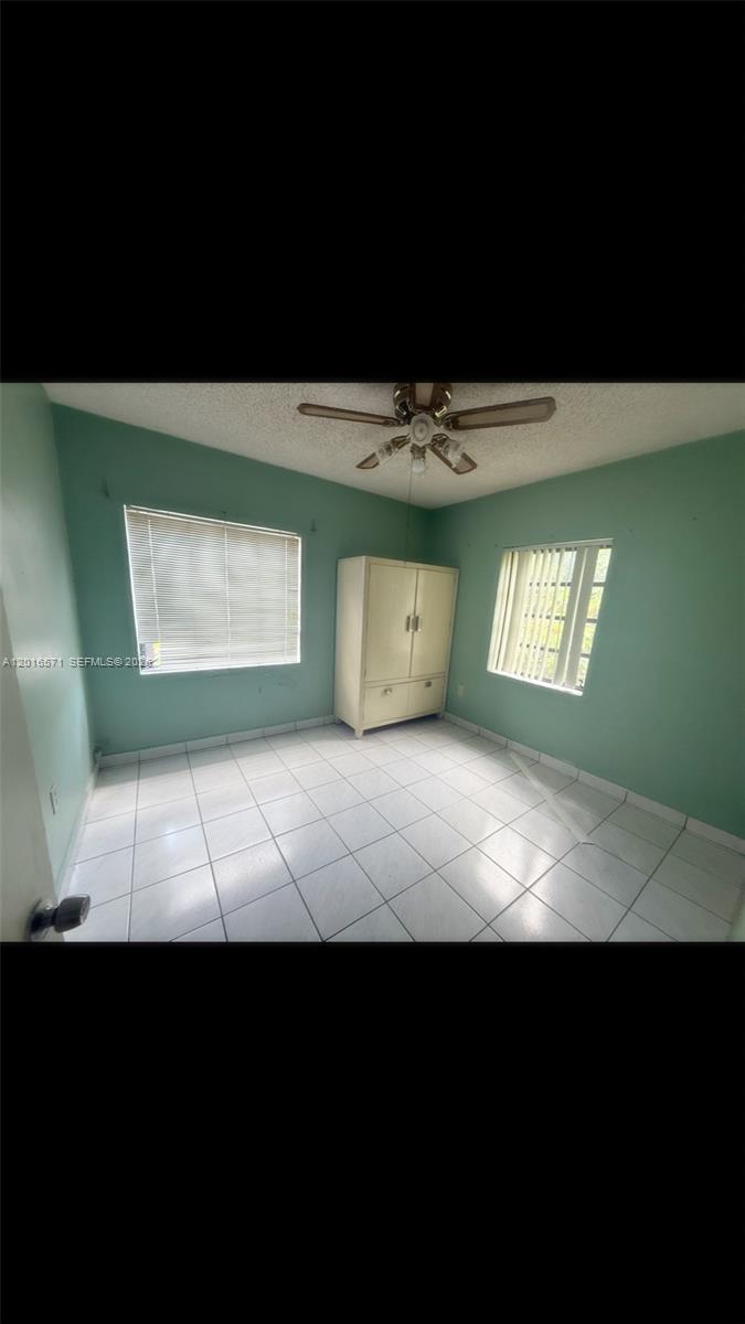 A bedroom with light green walls, white tile flooring, a ceiling fan, and a wardrobe — 50 E 44th St, Hialeah FL 33013, HIALEAH, FL