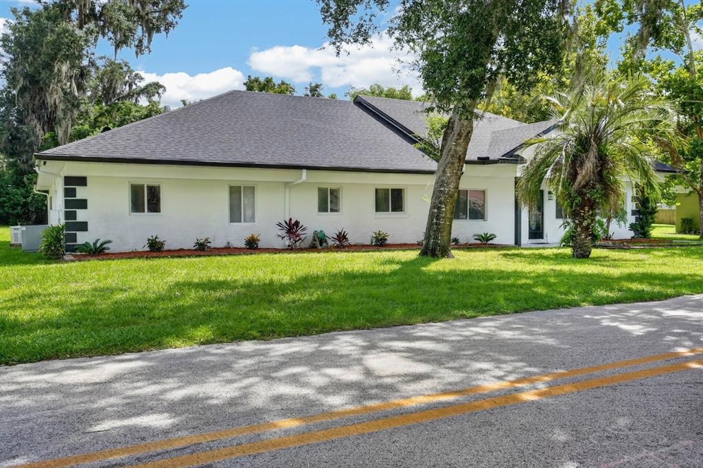 A white single-story house with a dark roof sits behind a lawn and paved road — 730 W UNIVERSITY AVENUE, DELAND, FL