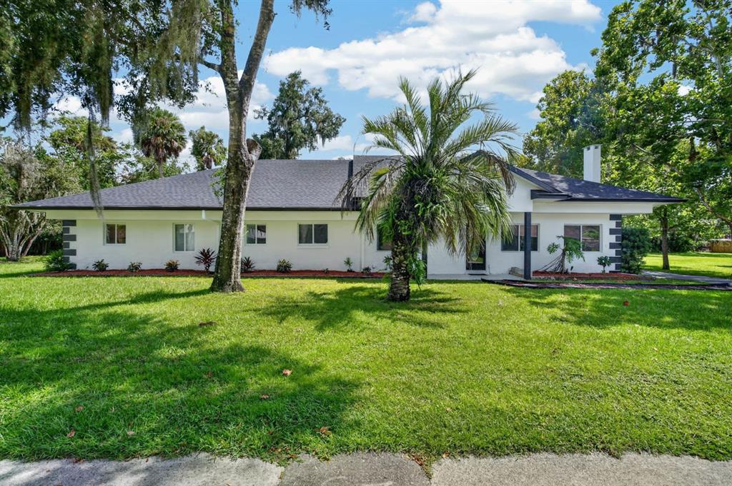 A single-story white house with a dark roof sits on a grassy lawn with trees — 730 W UNIVERSITY AVENUE, DELAND, FL