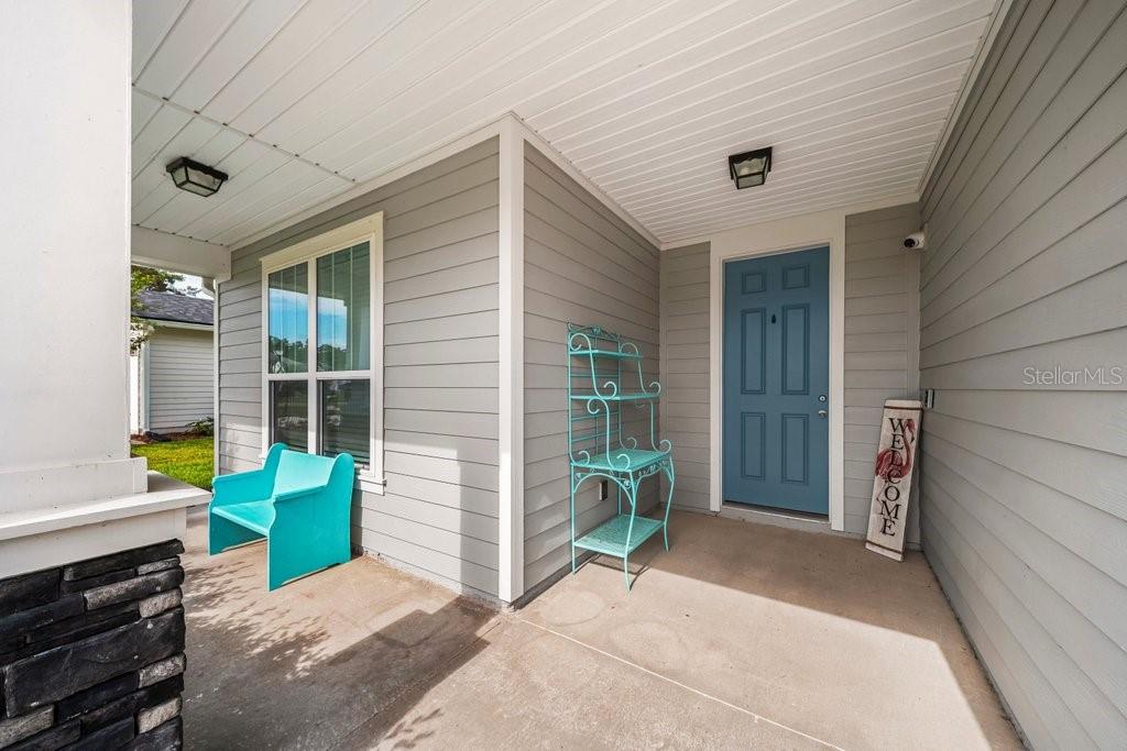 A covered front porch features gray siding, a blue door, a turquoise chair, and shelving — 338 WILLOW LAKE DRIVE, ST AUGUSTINE, FL