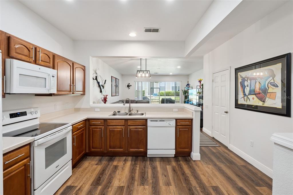 A kitchen with wood cabinets, white appliances, and wood-look flooring opens to a living area — 2521 GALLIANO CIRCLE, WINTER PARK, FL