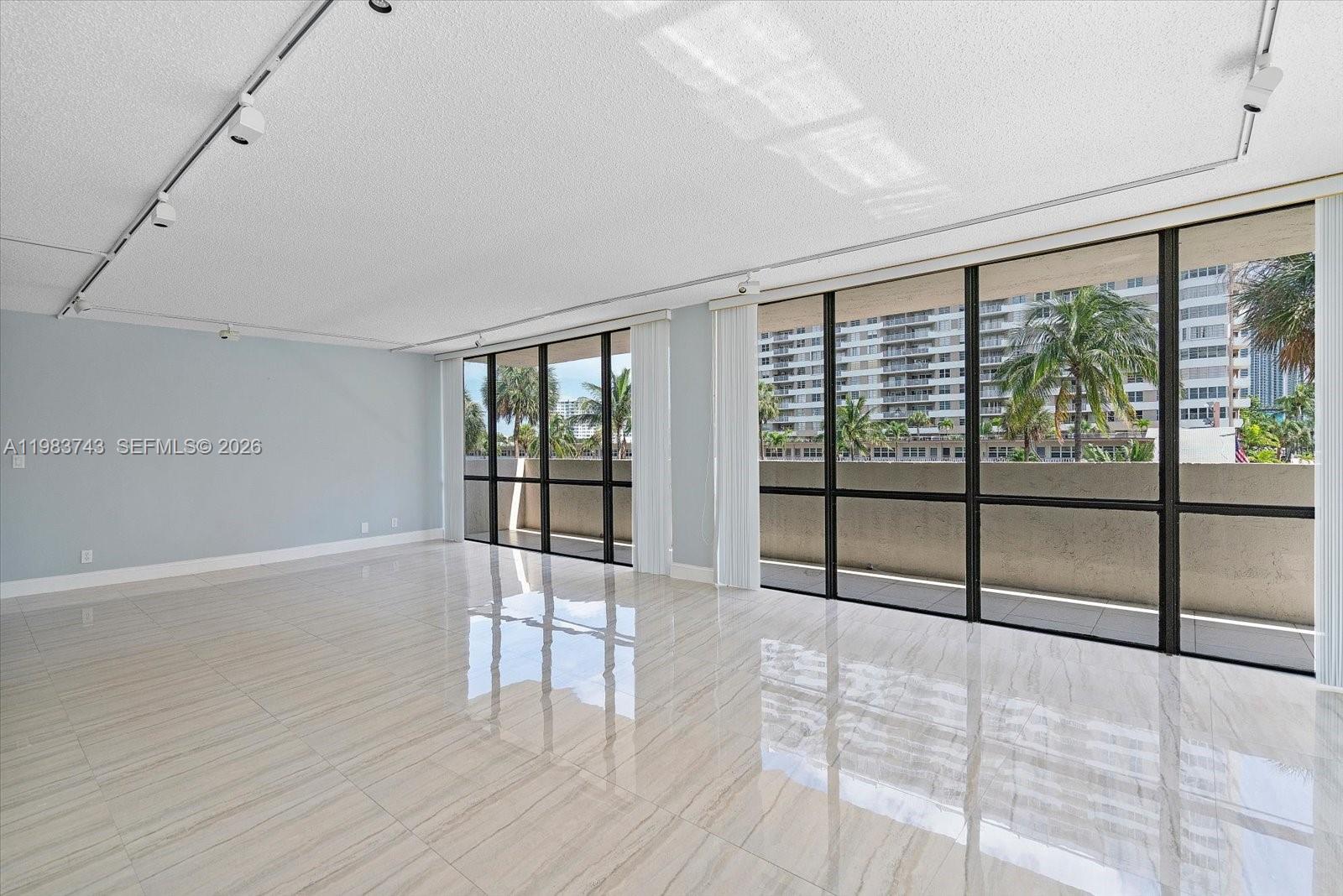 An empty room features light-colored tile floors, light blue walls, and floor-to-ceiling windows — 2049 S Ocean Dr # 210, Hallandale Beach FL 33009, HALLANDALE BEACH, FL