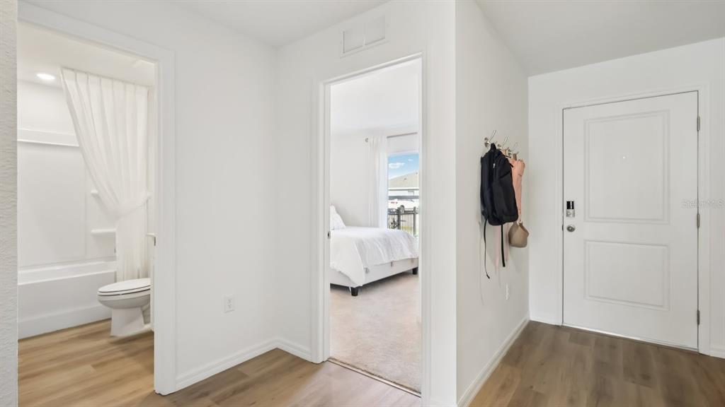 A hallway with wood-look flooring leads to a bathroom and a bedroom with white bedding — 1013 GUM SPRING COURT, RUSKIN, FL