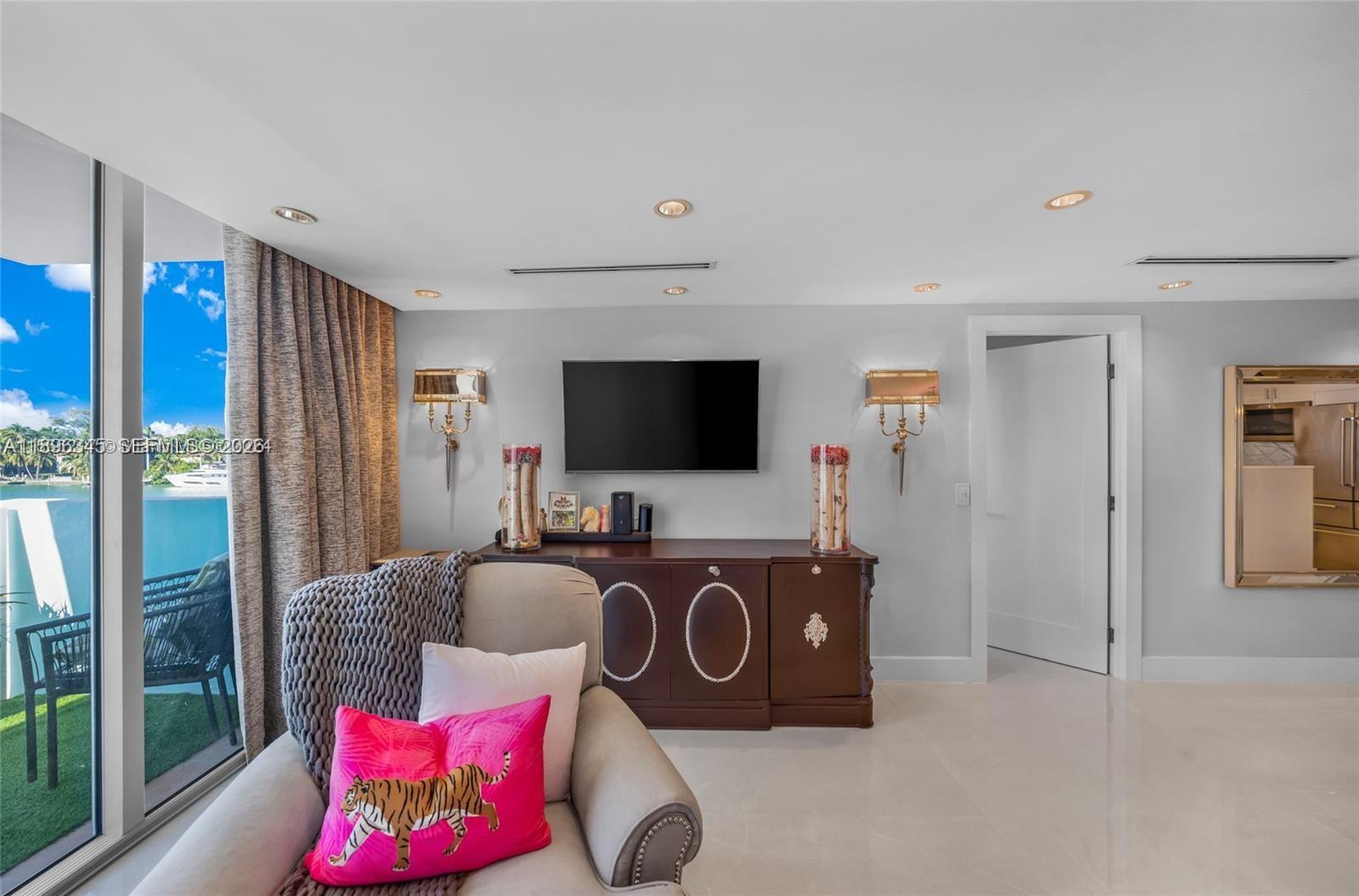 A living room features a television, dark wood console, wall sconces, and a waterfront view — 5838 Collins Ave # 2F, Miami Beach FL 33140, MIAMI BEACH, FL