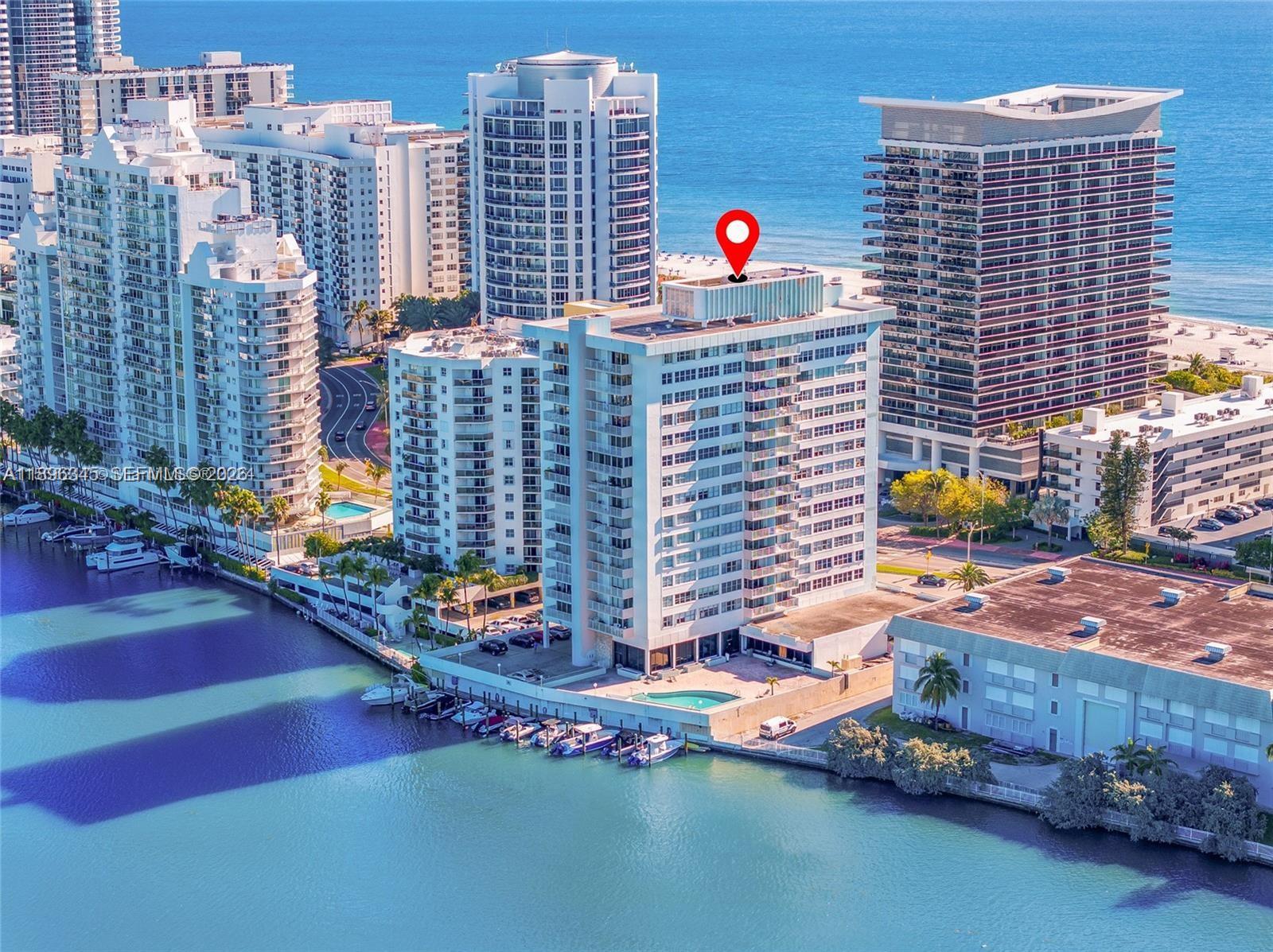 An aerial view of a white high-rise residential building situated along a waterfront with boats — 5838 Collins Ave # 2F, Miami Beach FL 33140, MIAMI BEACH, FL