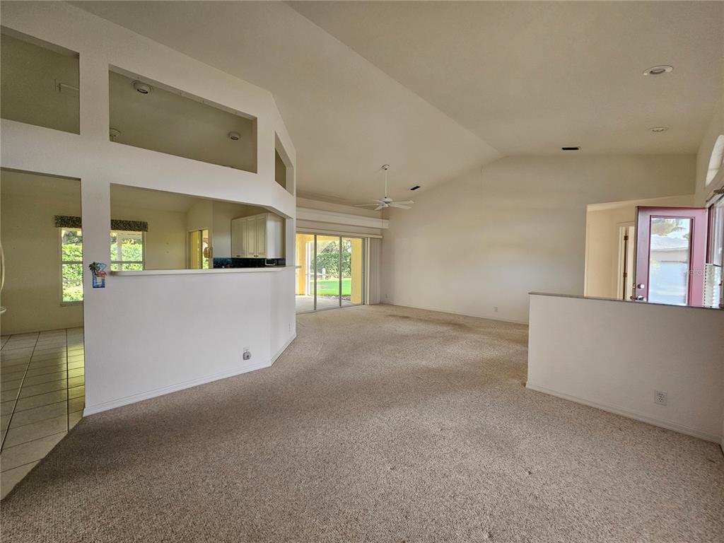 A spacious living room features beige carpeting, vaulted ceilings, and a partial wall partition — 6628 DEERING CIRCLE, SARASOTA, FL