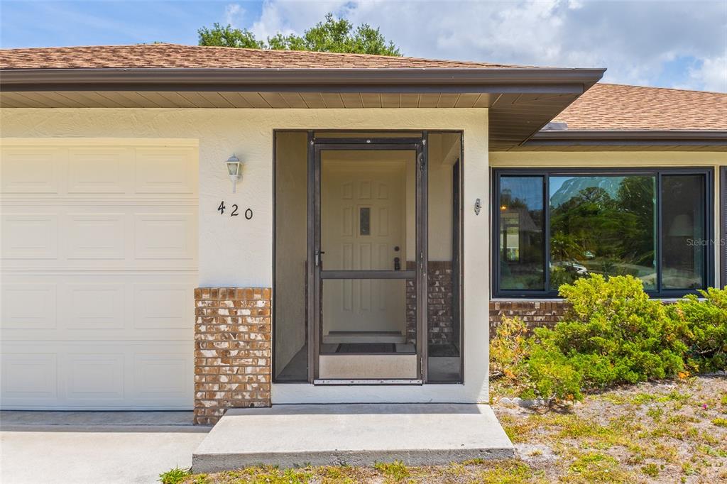 The exterior of a house features a garage, a screened front door, and brick accents — 420 DUKE ROAD, VENICE, FL