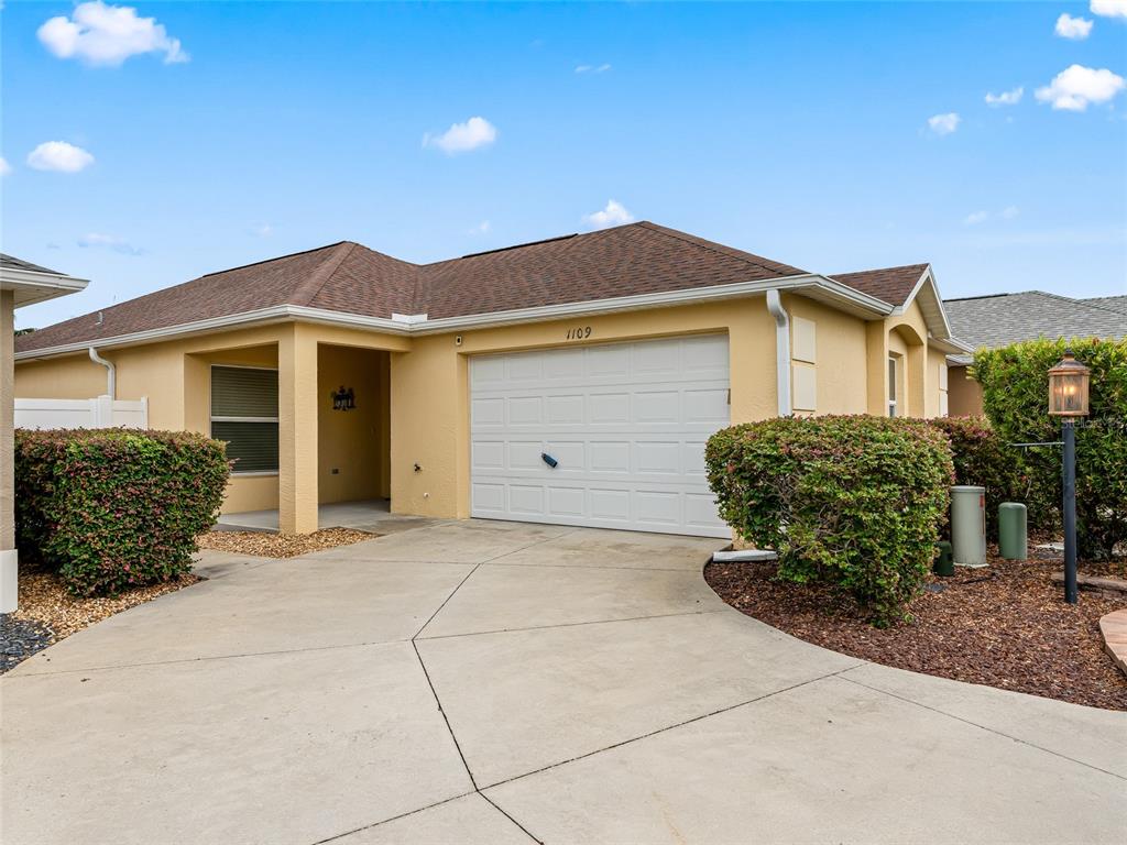 A single-story house with a yellow stucco exterior, a two-car garage, and landscaped bushes — 1109 TIPTON LANE, THE VILLAGES, FL