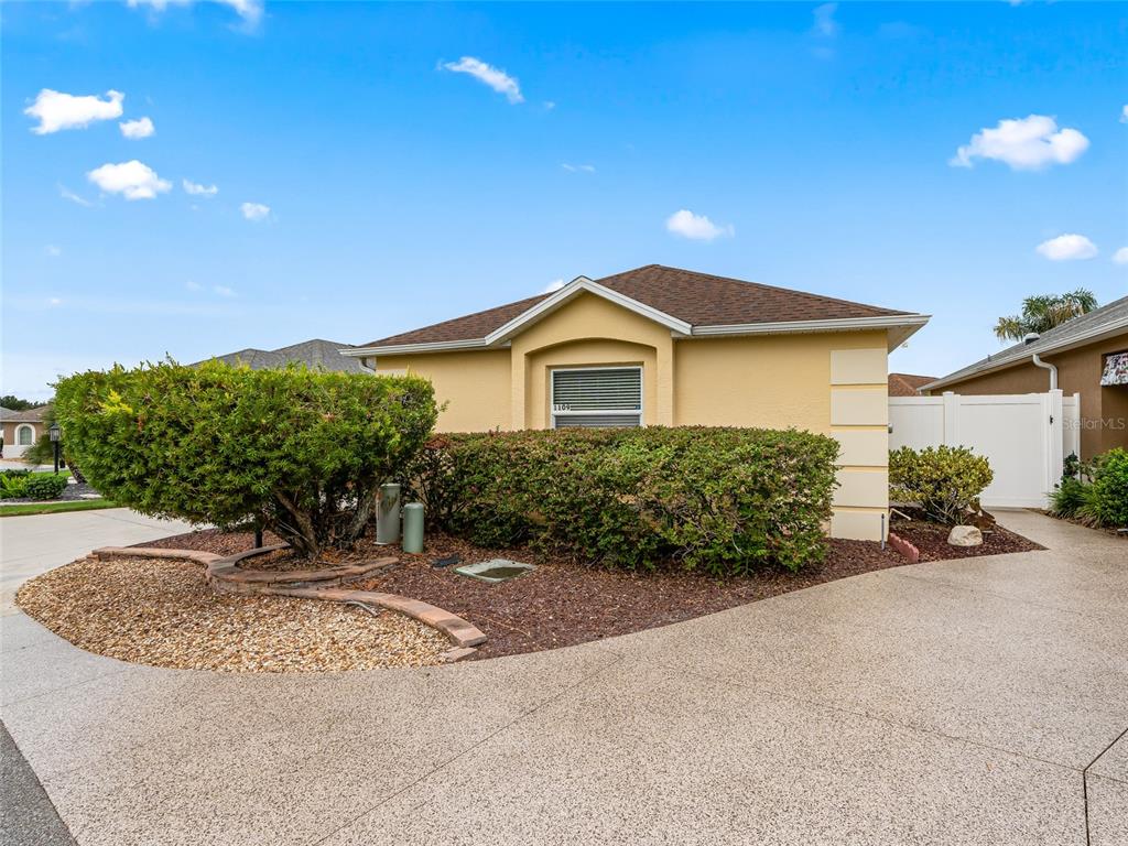 A tan single-story house features a large front hedge, a curved stone border, and driveway — 1109 TIPTON LANE, THE VILLAGES, FL
