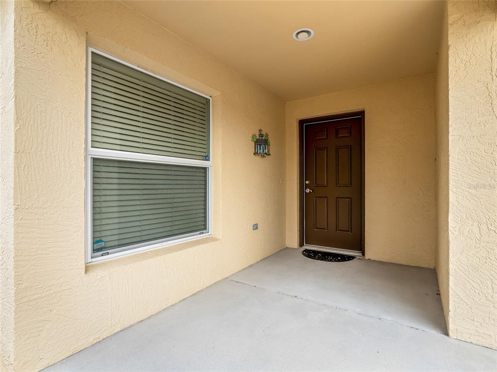 A covered entryway features a brown front door, a large window with blinds, and stucco walls — 1109 TIPTON LANE, THE VILLAGES, FL